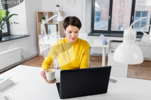 Image of businesswoman with laptop drinks coffee at office