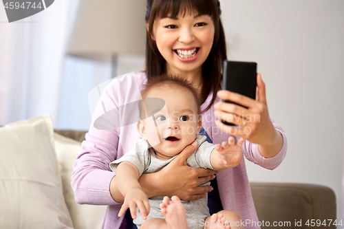 Image of asian mother with baby son taking selfie at home