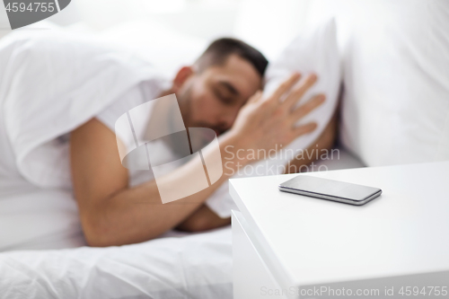 Image of smartphone on bedside table near sleeping man