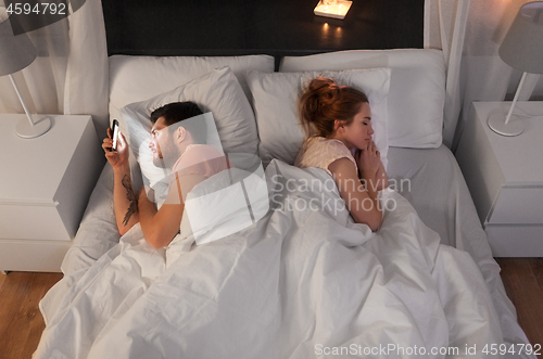 Image of man using smartphone while girlfriend is sleeping