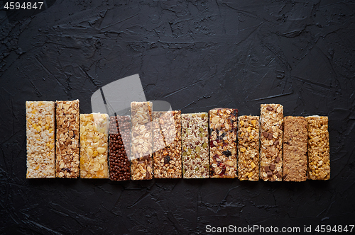 Image of Various healthy granola bars placed in a row on black stone tabl