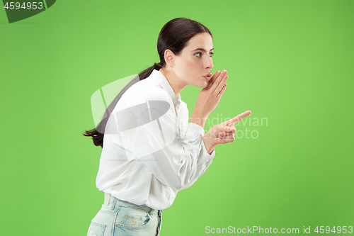 Image of The young woman whispering a secret behind her hand over green background