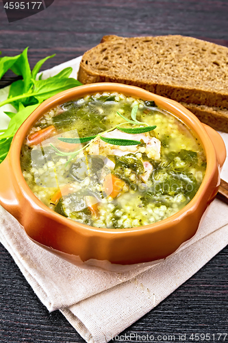 Image of Soup with couscous and spinach in clay bowl on board