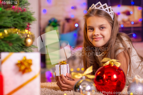 Image of The girl is lying at the Christmas tree and holding a small gift