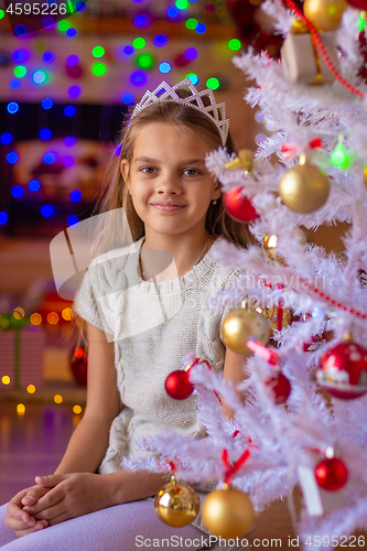 Image of Beautiful girl sits at the Christmas tree against the background of blurred lights