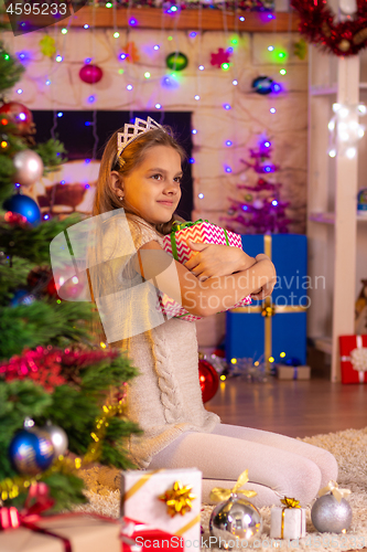 Image of Ten-year-old girl sits at the Christmas tree and hugs a gift