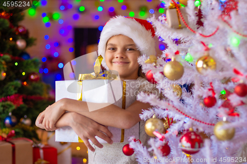 Image of Happy beautiful girl with a gift at a white Christmas tree