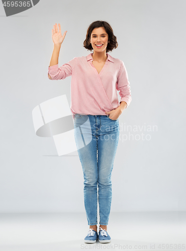 Image of young woman in shirt and jeans waving hand