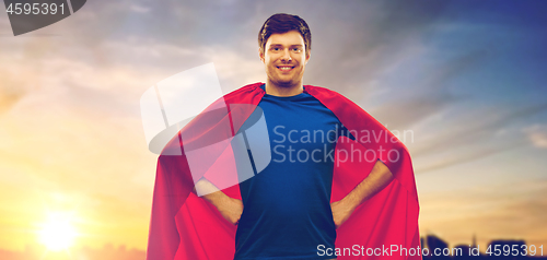 Image of man in red superhero cape over sunset in city