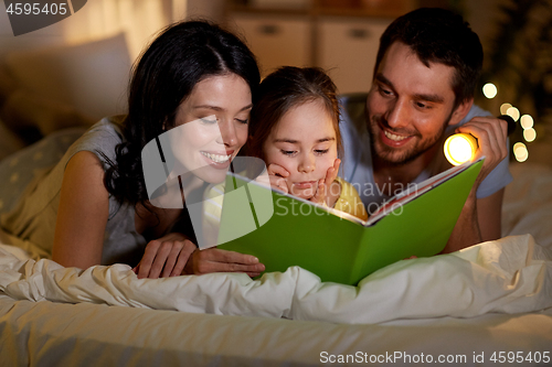 Image of happy family reading book in bed at night at home