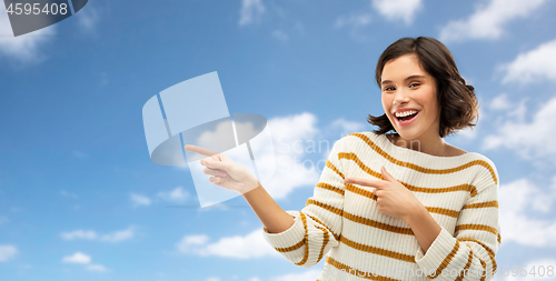 Image of happy woman pointing fingers to something over sky