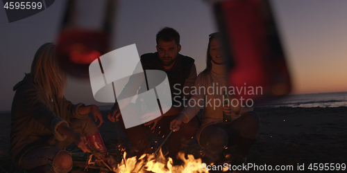 Image of Young Friends Making A Toast With Beer Around Campfire at beach