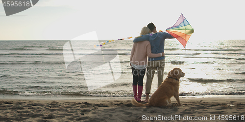 Image of couple with dog having fun on beach on autmun day