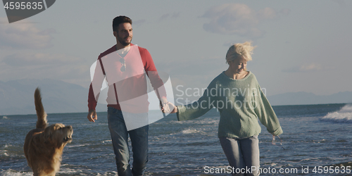 Image of couple with dog having fun on beach on autmun day