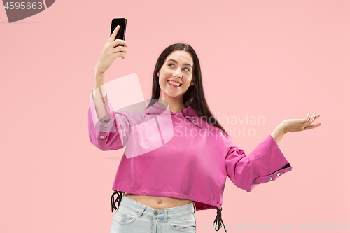 Image of Portrait of a happy smiling casual girl showing blank screen mobile phone isolated over pink background