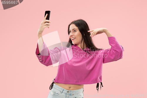 Image of Portrait of a happy smiling casual girl showing blank screen mobile phone isolated over pink background