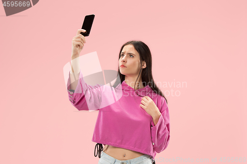 Image of Portrait of a happy smiling casual girl showing blank screen mobile phone isolated over pink background