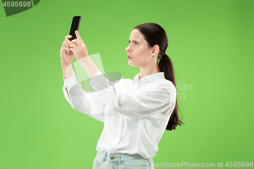 Image of Portrait of a happy smiling casual girl showing blank screen mobile phone isolated over green background