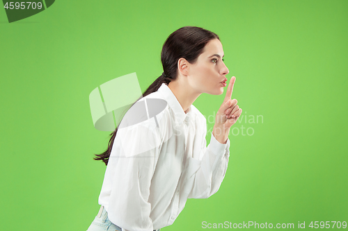 Image of The young woman whispering a secret behind her hand over green background