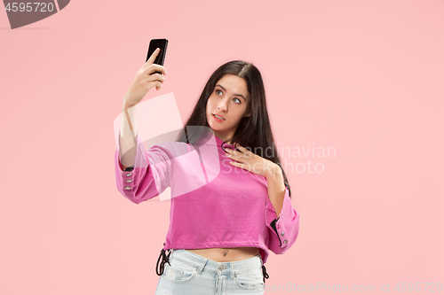 Image of Portrait of a happy smiling casual girl showing blank screen mobile phone isolated over pink background