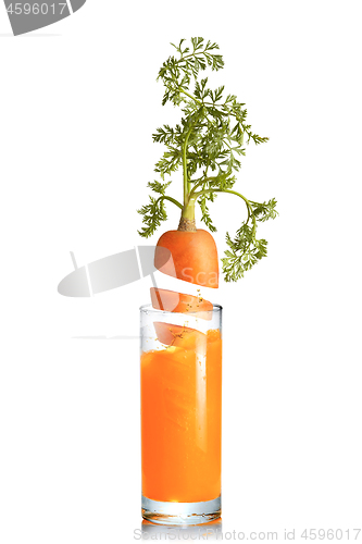 Image of Carrot root falls in a glass of fresh juice.