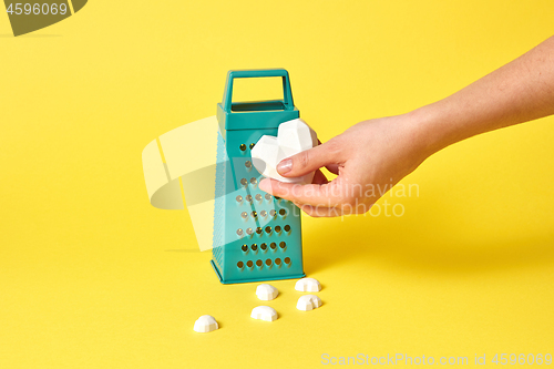 Image of Woman\'s hand holds plaster heart against kitchen grater.