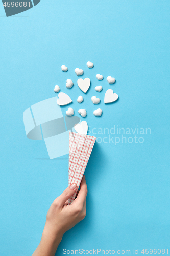 Image of Woman\'s hand with paper cone of small plaster hearts.