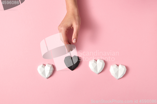 Image of Woman\'s hand puts black heart around white hearts.