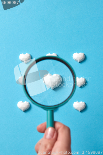 Image of Woman\'s hand holds big loupe above heart pattern.