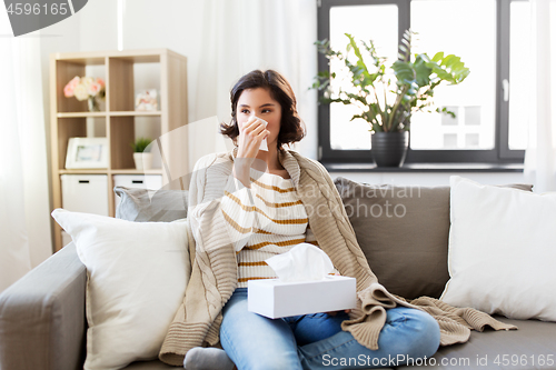 Image of sick woman blowing nose in paper tissue at home