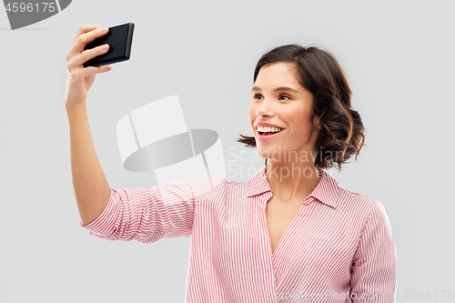 Image of smiling young woman taking selfie by smartphone