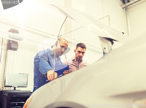 Image of auto mechanic with clipboard and man at car shop