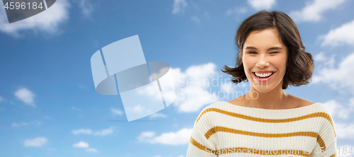 Image of happy smiling woman winking over blue sky