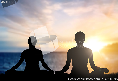 Image of couple doing yoga in lotus pose over sea sunset