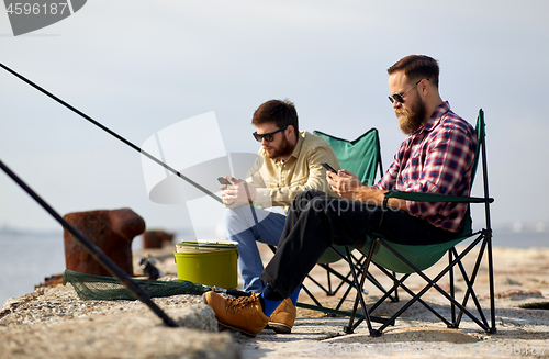 Image of friends with smartphones fishing on pier at sea