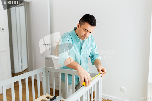 Image of father with tablet pc and ruler measuring baby bed