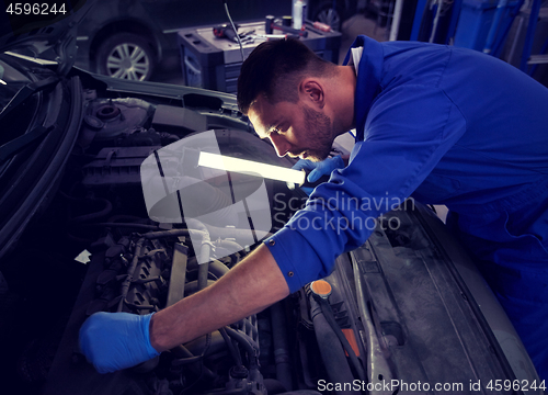 Image of mechanic man with lamp repairing car at workshop