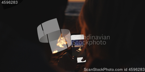 Image of Couple taking photos beside campfire on beach