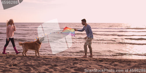 Image of couple with dog having fun on beach on autmun day