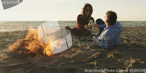 Image of Loving Young Couple Sitting On The Beach beside Campfire drinkin