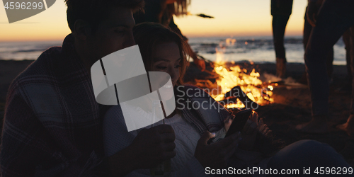 Image of Couple enjoying bonfire with friends on beach