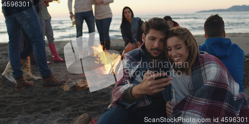 Image of Couple enjoying bonfire with friends on beach