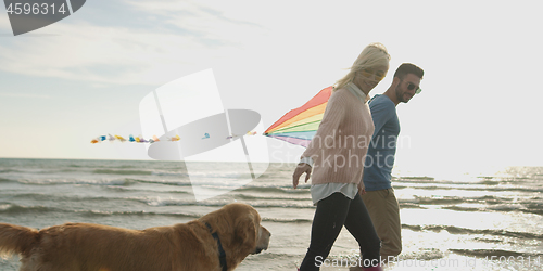 Image of couple with dog having fun on beach on autmun day