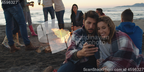 Image of Couple enjoying bonfire with friends on beach