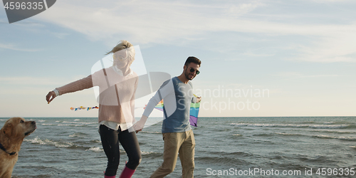 Image of couple with dog having fun on beach on autmun day