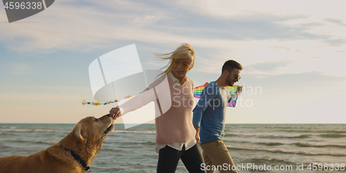 Image of couple with dog having fun on beach on autmun day