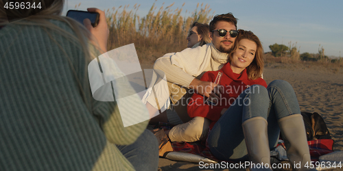 Image of Loving Young Couple Sitting On The Beach beside Campfire drinkin