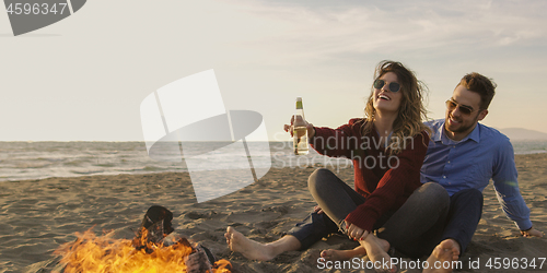 Image of Loving Young Couple Sitting On The Beach beside Campfire drinkin