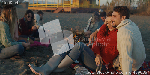 Image of Loving Young Couple Sitting On The Beach beside Campfire drinkin