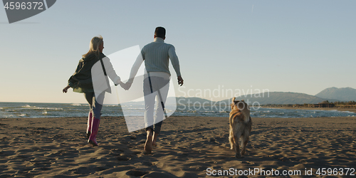 Image of couple with dog having fun on beach on autmun day